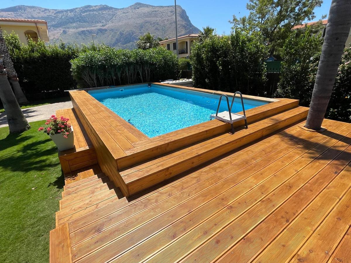 Piscina fuori terra rivestita in legno, con piano di calpestio e gradini che scendono sul prato
